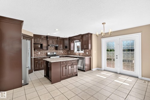 Spacious kitchen featuring dark wood cabinetry, a central island with a light-toned countertop, and a mosaic tile backsplash - 4711 152 Avenue Nw, Edmonton, AB 