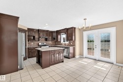 Spacious kitchen featuring dark wood cabinetry, a central island with a light-toned countertop, and a mosaic tile backsplash - 