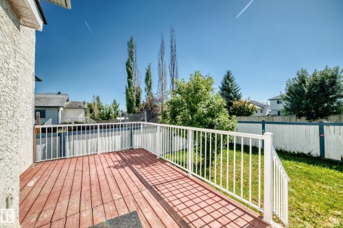 Spacious wood-finish deck with white railings, offering direct access to the backyard with a grass lawn and established perimeter fencing - 4711 152 Avenue Nw, Edmonton, AB 