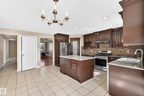 Kitchen featuring dark wood-finish cabinetry, a central island, stainless steel appliances, a tile backsplash, and light tile flooring - 4711 152 Avenue Nw, Edmonton, AB 