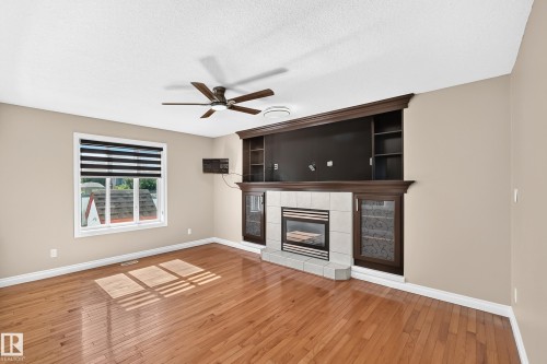 Hardwood flooring, recessed fireplace with tile surround, built-in entertainment center with shelving, ceiling fan, and window with blinds - 4711 152 Avenue Nw, Edmonton, AB 