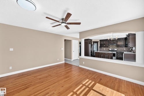 Hardwood flooring, arched pass-through, dark wood-finish cabinetry, stainless steel appliances, and ceiling fan with integrated lighting - 4711 152 Avenue Nw, Edmonton, AB 
