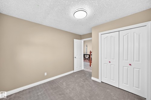 Neutral tone wall paint, textured ceiling, flush mount ceiling light, white bi-fold doors, and gray carpet flooring - 4711 152 Avenue Nw, Edmonton, AB 