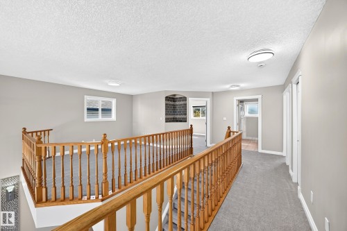 Generous upper-level landing featuring warm wood railings with turned balusters, recessed ceiling lighting, and neutral carpeting - 4711 152 Avenue Nw, Edmonton, AB 