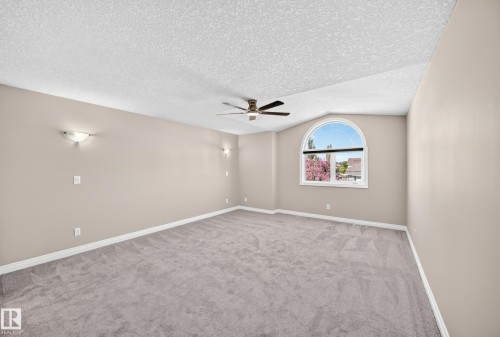 Arched window, ceiling fan, wall sconces, neutral paint, and carpeted flooring - 4711 152 Avenue Nw, Edmonton, AB 