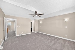 Spacious room with sloped ceiling, ceiling fan, neutral wall paint, and wall-mounted light fixtures - 
