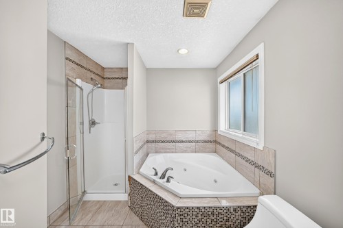 Corner jetted tub with tile surround, glass-enclosed shower, and a window with privacy blinds - 4711 152 Avenue Nw, Edmonton, AB 