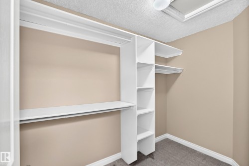 Custom closet system with multiple white shelves and hanging rods, beige wall paint, and gray carpet flooring - 4711 152 Avenue Nw, Edmonton, AB 