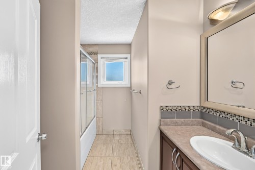 Bathroom vanity with integrated sink, mosaic tile backsplash, and mirror with overhead lighting - 4711 152 Avenue Nw, Edmonton, AB 