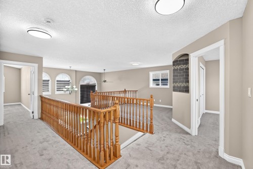 Carpeted upper landing with wood railings, arched windows, and a decorative tiled wall niche - 4711 152 Avenue Nw, Edmonton, AB 