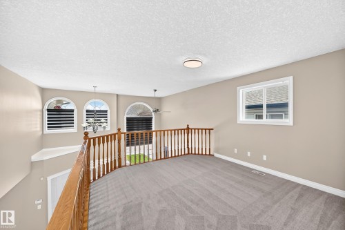 Carpeted loft area with wood-finish railing, flush-mount ceiling light, and arched windows - 4711 152 Avenue Nw, Edmonton, AB 