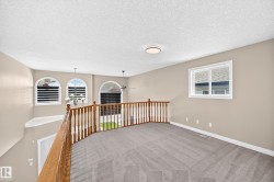 Carpeted loft area with wood-finish railing, flush-mount ceiling light, and arched windows - 
