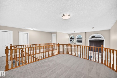 Spacious carpeted loft with wood-finish railings, recessed lighting, and arched windows featuring blinds - 4711 152 Avenue Nw, Edmonton, AB 