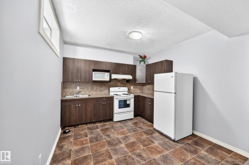 Kitchen featuring dark wood-finish cabinetry, white appliances, speckled countertops, and a tiled floor - 4711 152 Avenue Nw, Edmonton, AB 