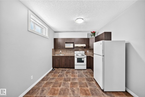 Compact kitchen area featuring dark wood-finish cabinetry, a white electric range, a white refrigerator, and durable tile-patterned flooring - 4711 152 Avenue Nw, Edmonton, AB 