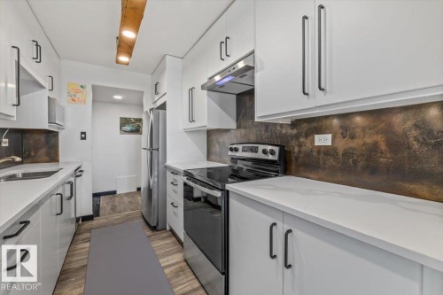 Galley kitchen with white cabinetry, stainless steel appliances, white countertops, and a textured backsplash - #906 12303 Jasper Av Nw, Edmonton, AB 
