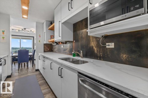 Kitchen featuring light cabinetry with black hardware, stainless steel sink, integrated dishwasher, and a built-in microwave - #906 12303 Jasper Av Nw, Edmonton, AB 