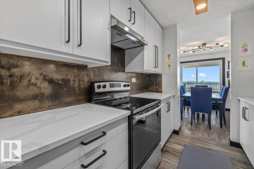 White cabinetry with black hardware, an integrated range hood, white countertops, and a textured backsplash, with wood-finish flooring - #906 12303 Jasper Av Nw, Edmonton, AB 