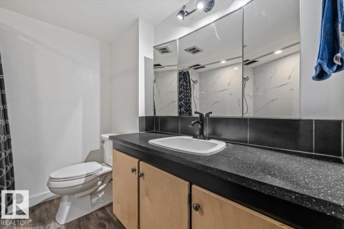 Vanity with integrated sink, black speckled countertop, wood-finish cabinetry, and dark bronze faucet - #906 12303 Jasper Av Nw, Edmonton, AB 
