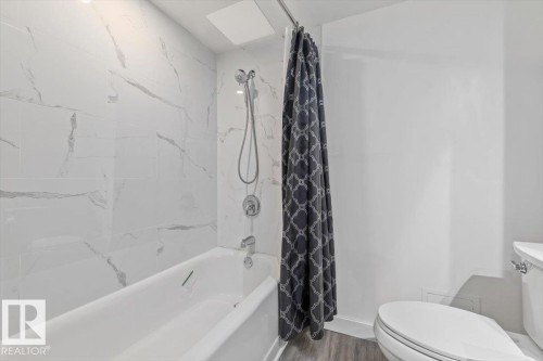 Bathtub with a shower fixture, white tile surround, and wood-finish flooring - #906 12303 Jasper Av Nw, Edmonton, AB 