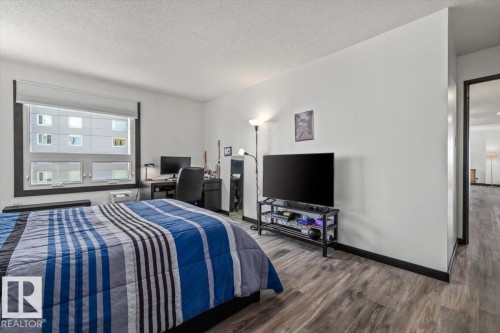 Spacious room featuring wood-finish flooring, a large window with roller shades, and ample wall space - #906 12303 Jasper Av Nw, Edmonton, AB 