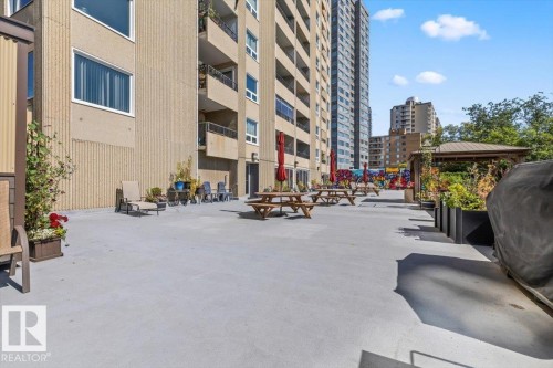 Expansive outdoor patio area featuring a pergola, multiple picnic tables, and planters with established greenery - #906 12303 Jasper Av Nw, Edmonton, AB 