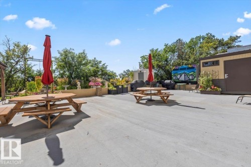Expansive paved patio area featuring a low retaining wall with plantings and mature trees - #906 12303 Jasper Av Nw, Edmonton, AB 