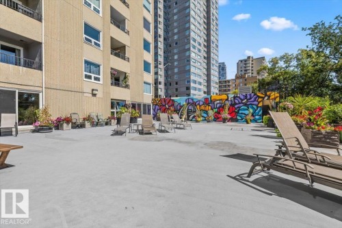 Rooftop patio with a concrete surface, mural, green landscaping, and building exterior - #906 12303 Jasper Av Nw, Edmonton, AB 