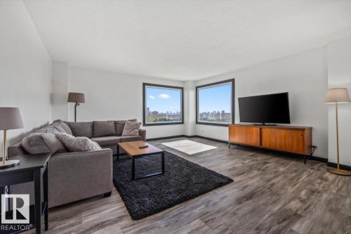 Expansive living area featuring wood-finish flooring, white walls, and multiple large windows with black trim - #906 12303 Jasper Av Nw, Edmonton, AB 