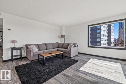Expansive living area featuring wood-finish flooring and a large picture window with dark trim - #906 12303 Jasper Av Nw, Edmonton, AB 