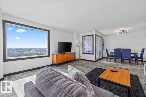 Expansive window offering a broad landscape, wood-finish flooring, recessed lighting, and a dining area with a modern chandelier - #906 12303 Jasper Av Nw, Edmonton, AB 
