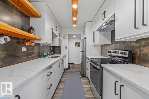 Galley kitchen featuring white cabinetry, light-toned countertops, a stainless steel refrigerator, and a black electric range with a coordinating range hood - #906 12303 Jasper Av Nw, Edmonton, AB 