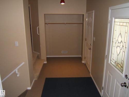 Entryway with an open closet featuring a hanging rod and upper shelf, a paneled door, a decorative glass-insert entry door, and a staircase with a handrail - 4825 59 Avenue, Vegreville, AB 