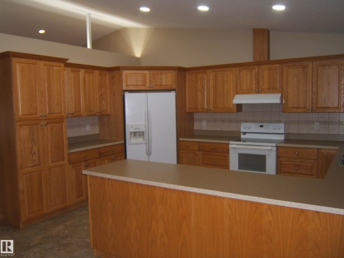 Vaulted ceiling with recessed lighting, wood-finish cabinetry, tile backsplash, and a built-in kitchen island with countertop - 4825 59 Avenue, Vegreville, AB 