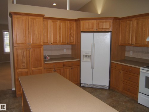 Kitchen featuring wood-finish cabinetry, a central island, laminate countertops, and tile flooring - 4825 59 Avenue, Vegreville, AB 