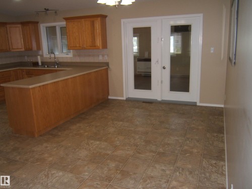Kitchen featuring wood-finish cabinetry, light-toned countertops, and a tiled backsplash - 4825 59 Avenue, Vegreville, AB 