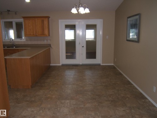 Kitchen area with wood-finish cabinetry, light-toned countertops, and a tiled backsplash - 4825 59 Avenue, Vegreville, AB 