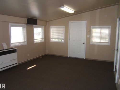 Neutral tone wall paint, dark floor carpeting, multiple windows, built-in air conditioning unit, and a standard white entry door - 4825 59 Avenue, Vegreville, AB 