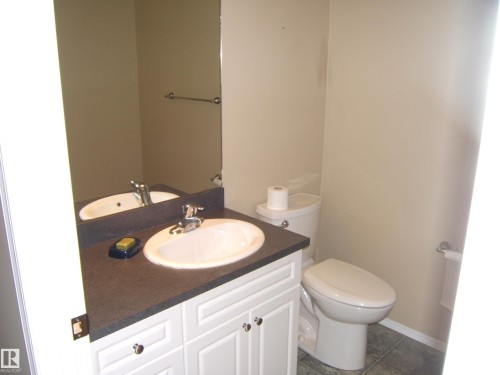 Vanity with a white basin and chrome faucet, dark countertop, and paneled white cabinetry - 4825 59 Avenue, Vegreville, AB 