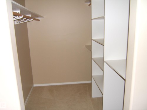 Walk-in closet featuring carpet flooring, built-in shelving, and a hanging rod - 4825 59 Avenue, Vegreville, AB 