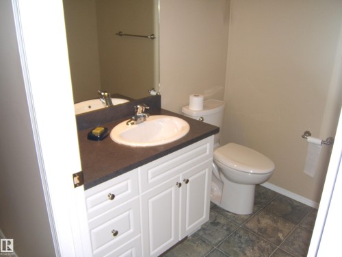 White cabinetry with knob hardware, dark countertop, ceramic sink with chrome faucet, wall-mounted mirror, and tile-finish flooring - 4825 59 Avenue, Vegreville, AB 