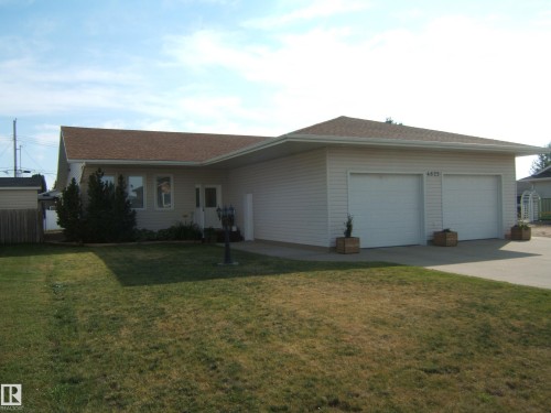 Single-story residence featuring light-colored siding, a brown shingle roof, a two-car garage, and a concrete driveway - 4825 59 Avenue, Vegreville, AB 