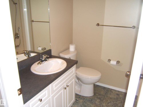 Vanity with white paneled cabinetry, integral basin, and dark countertop - 4825 59 Avenue, Vegreville, AB 