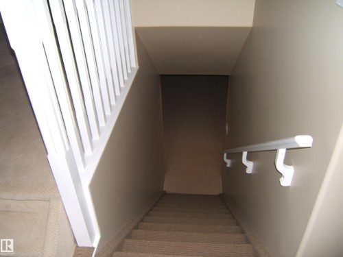 Carpeted staircase with white balusters and a wall-mounted handrail - 4825 59 Avenue, Vegreville, AB 