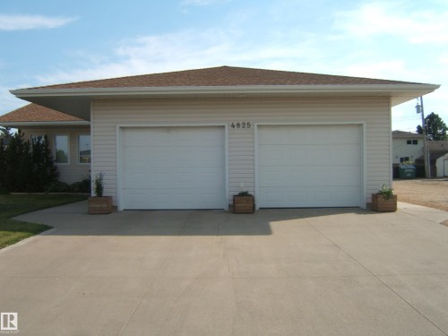 Two-car garage with white panel doors and an expansive concrete driveway - 4825 59 Avenue, Vegreville, AB 