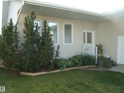 Manicured lawn with a defined garden bed featuring mature shrubs and hostas - 4825 59 Avenue, Vegreville, AB 