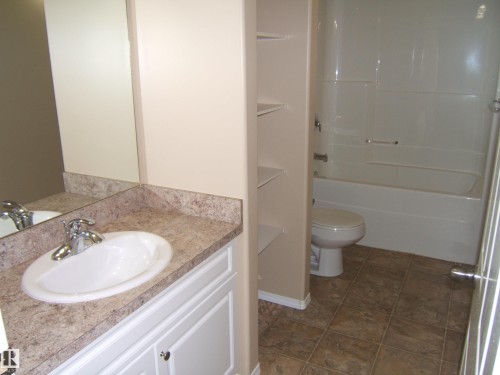 Vanity with an oval sink and a patterned countertop, integrated shelving, and a bathtub with a shower kit - 4825 59 Avenue, Vegreville, AB 