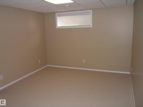 Neutral-toned walls with coordinated carpet flooring, drop ceiling with integrated lighting, and a window with blinds - 4825 59 Avenue, Vegreville, AB 