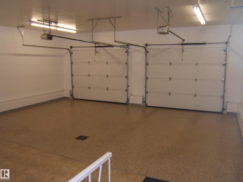 Two white overhead garage doors with automatic openers, a speckled epoxy floor coating, and fluorescent ceiling lights - 4825 59 Avenue, Vegreville, AB 