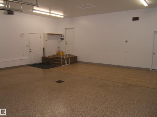 Spacious garage with durable epoxy flooring, overhead fluorescent lighting, and a built-in elevated platform - 4825 59 Avenue, Vegreville, AB 